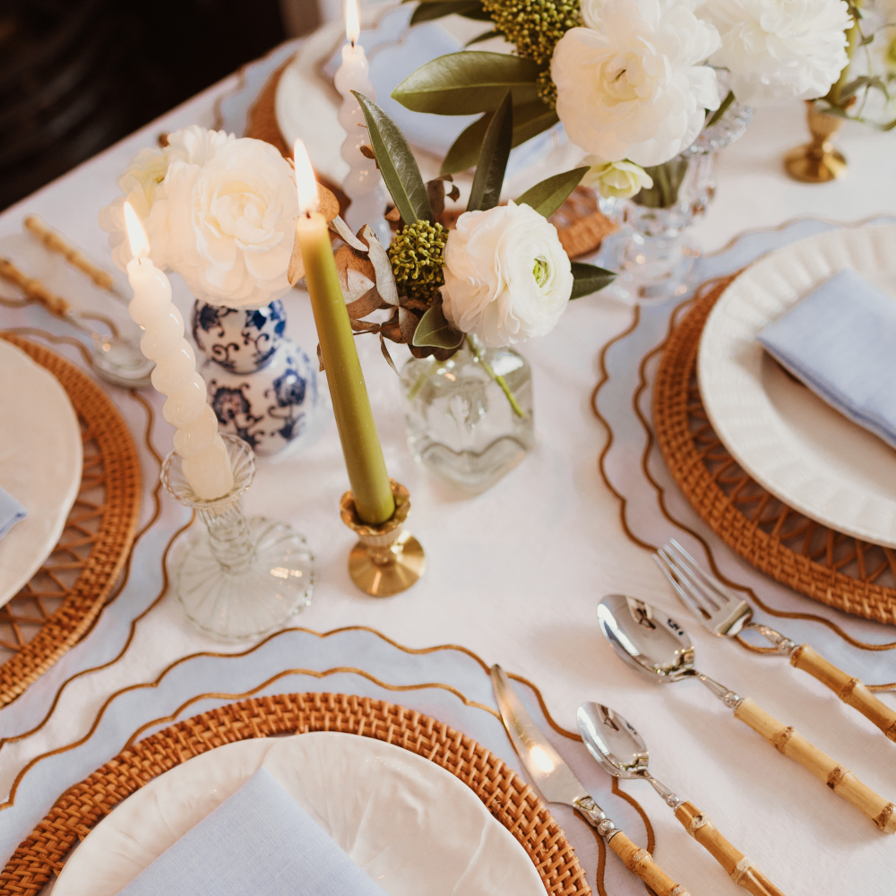 Elegant table setting with candles, flowers, and cutlery on a white tablecloth.
