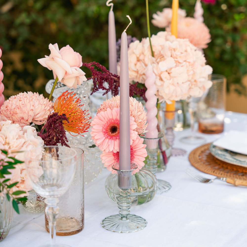 Decorative table setting with flowers, candles, and glassware on a white tablecloth.