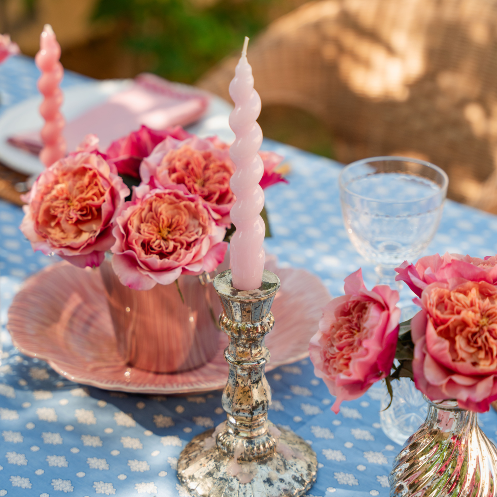Decorative table setting with pink candles, flowers, and a glass on a polka dot tablecloth.