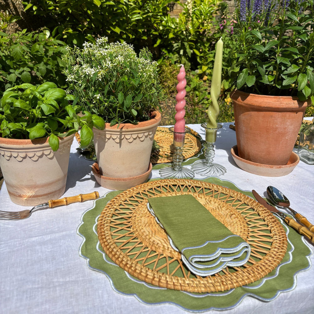 Outdoor table setting with woven placemat, green napkin, and potted plants.