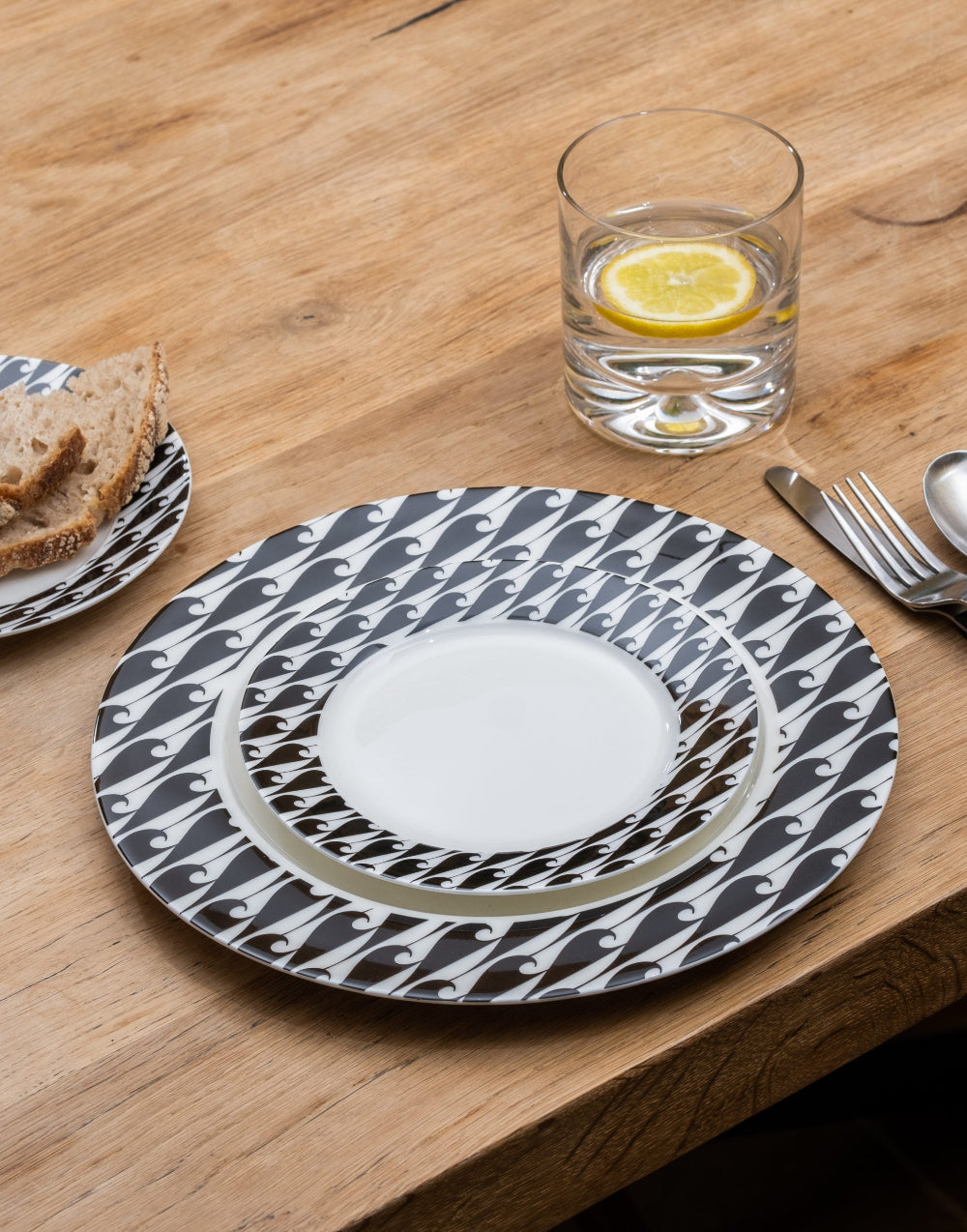 Dinner setting with a patterned wave plate, glass of water and lemon slice on a wooden table.