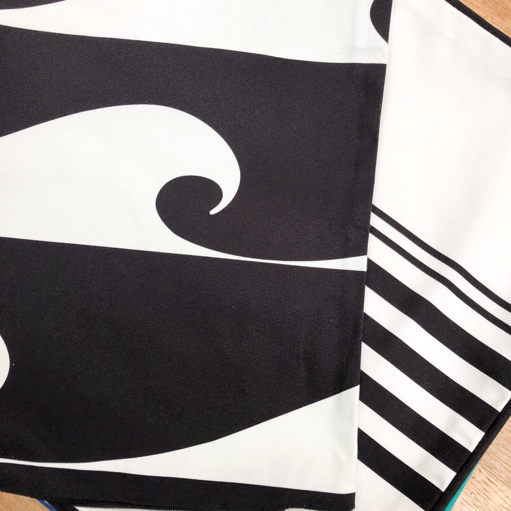 Black and white cushion cover with wave and striped design on a wooden surface