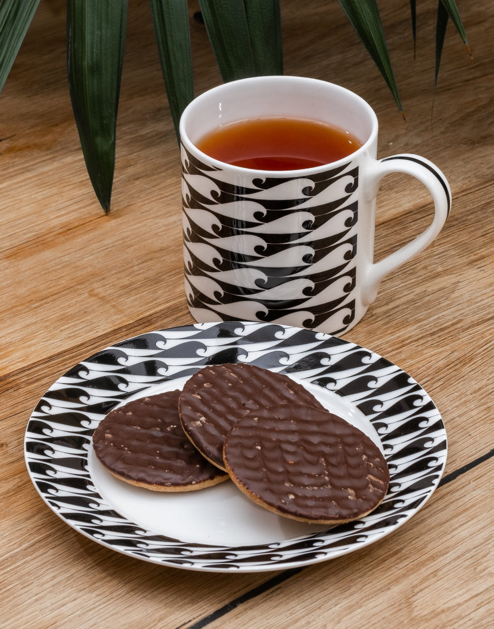 Cup of tea with cookies on a matching plate with black waves on a wooden surface