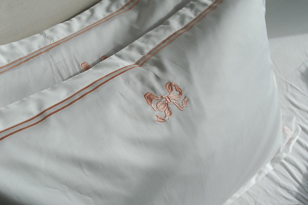 Close-up of white pillowcases with peach bow design embroidery on a light background