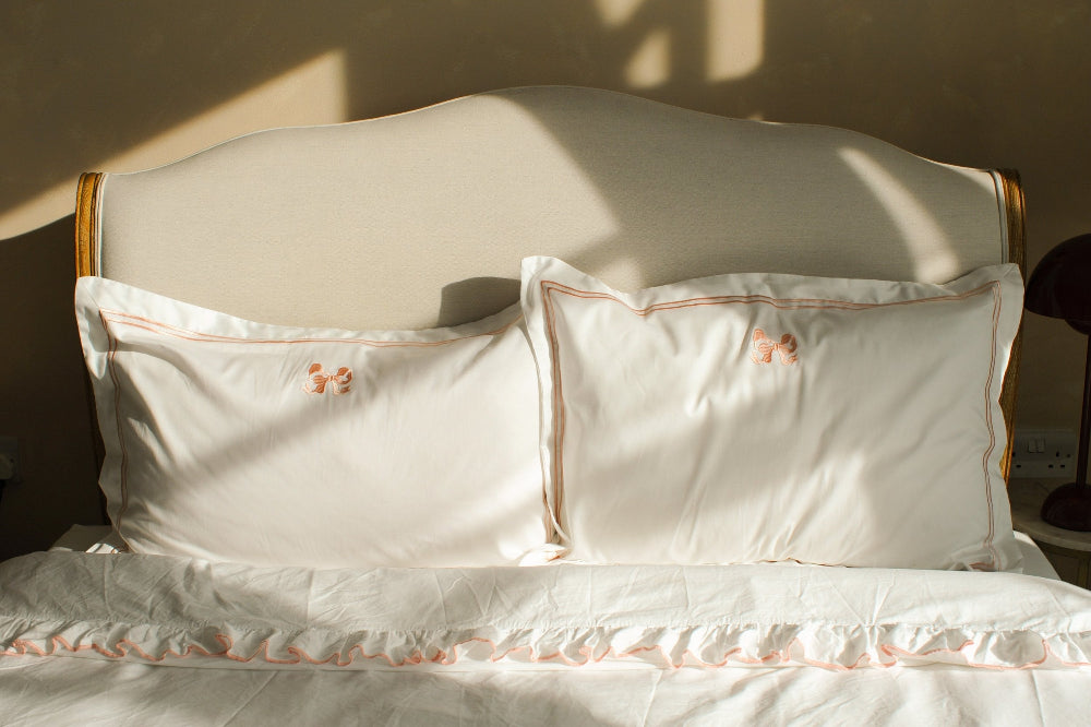 White pillows with pink embroidery on a bed with a wooden headboard.