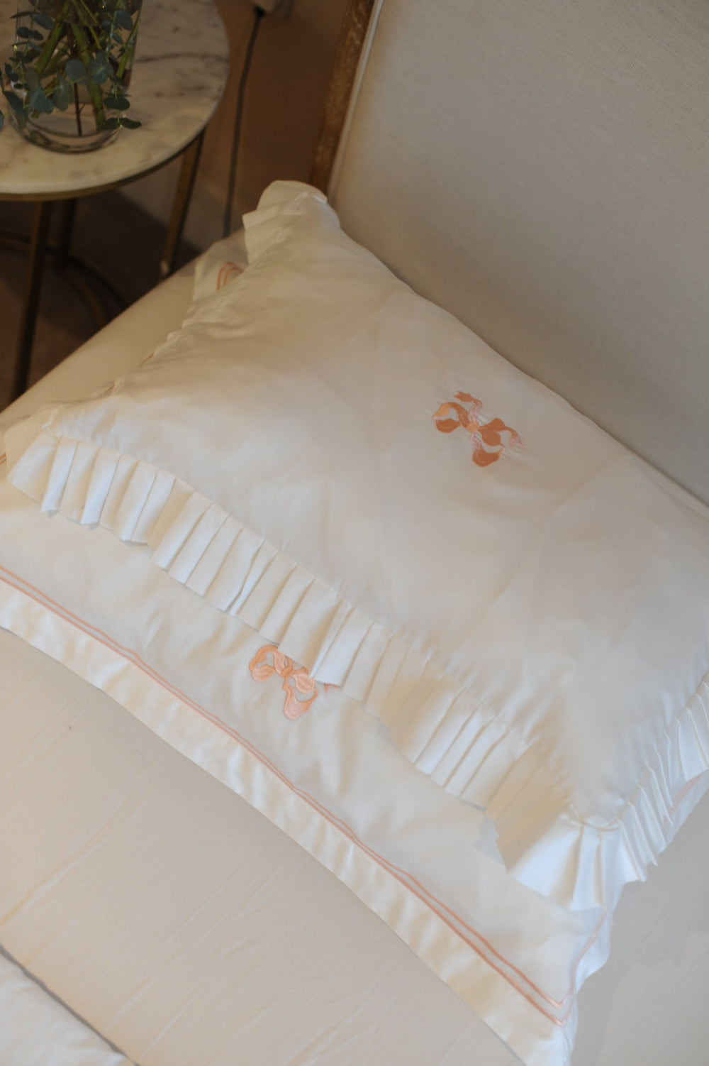 White pillow with bow embroidery on a bed in a bedroom setting.