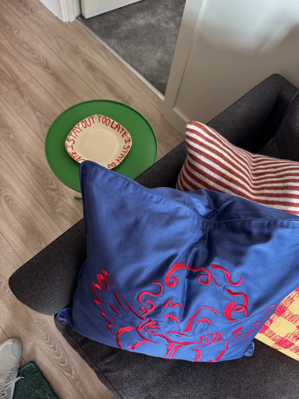 Blue cushion with red embroidered cherub on a chair next to a striped pillow