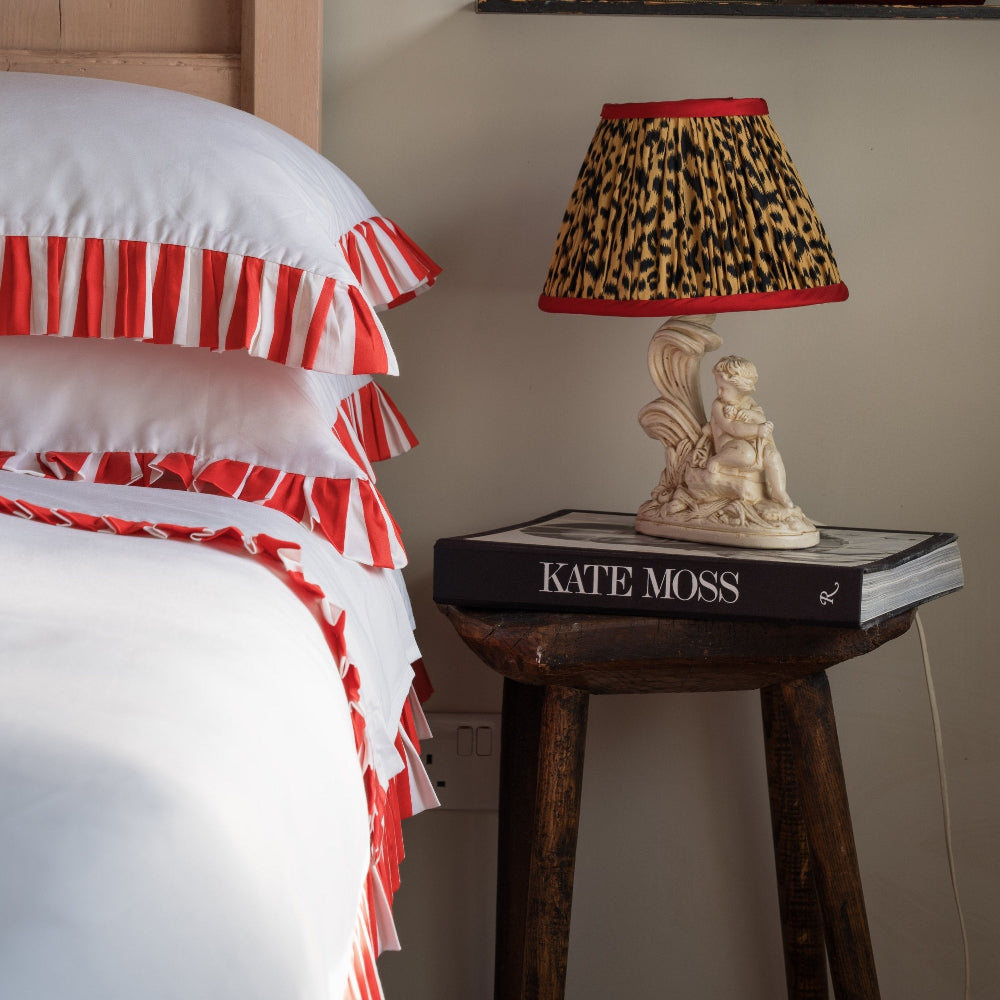 Bed with red and white striped bedding, nightstand with lamp and book titled 'Kate Moss'.