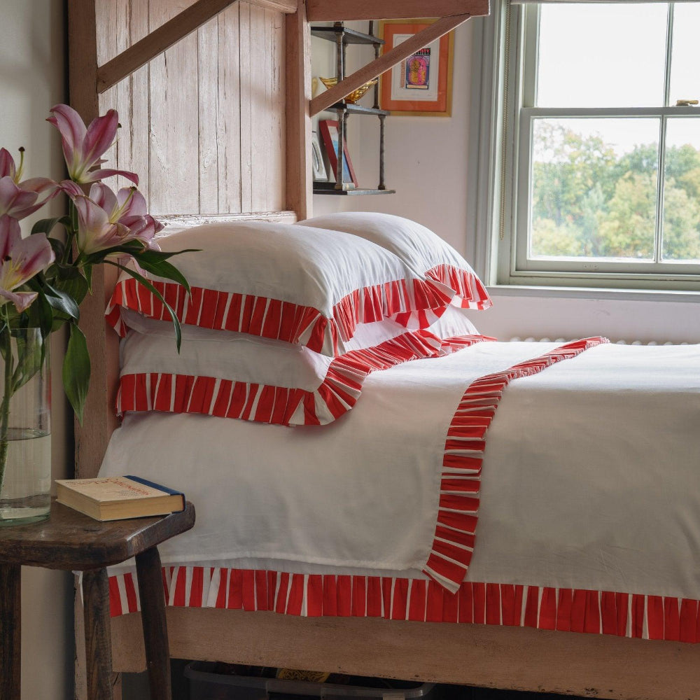 Bed with red and white striped bedding in a room with a window and side table.