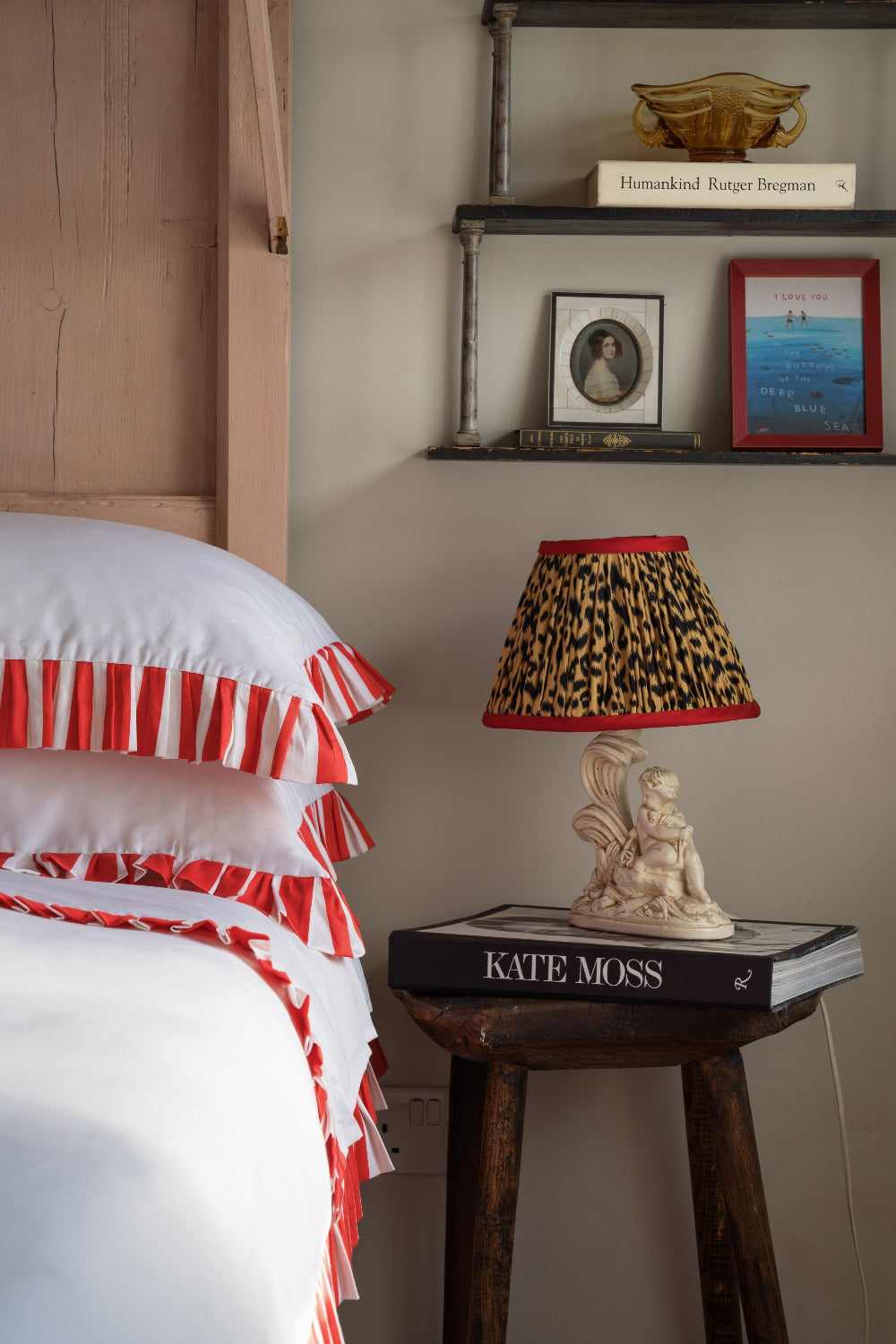 Bedroom scene with a lamp on a small table, books, and decorative items.