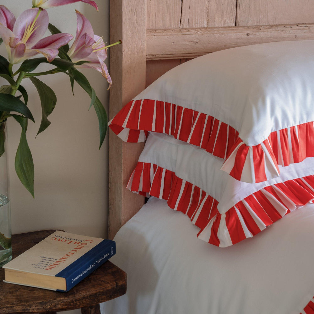 Red and white striped pillow on a bed next to a wooden nightstand with a book and plant.