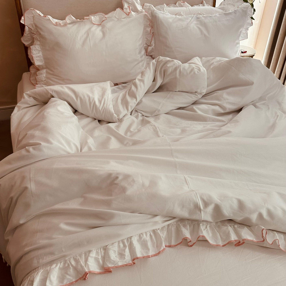 White bedspread with pink ruffled edges on a bed in a softly lit room.