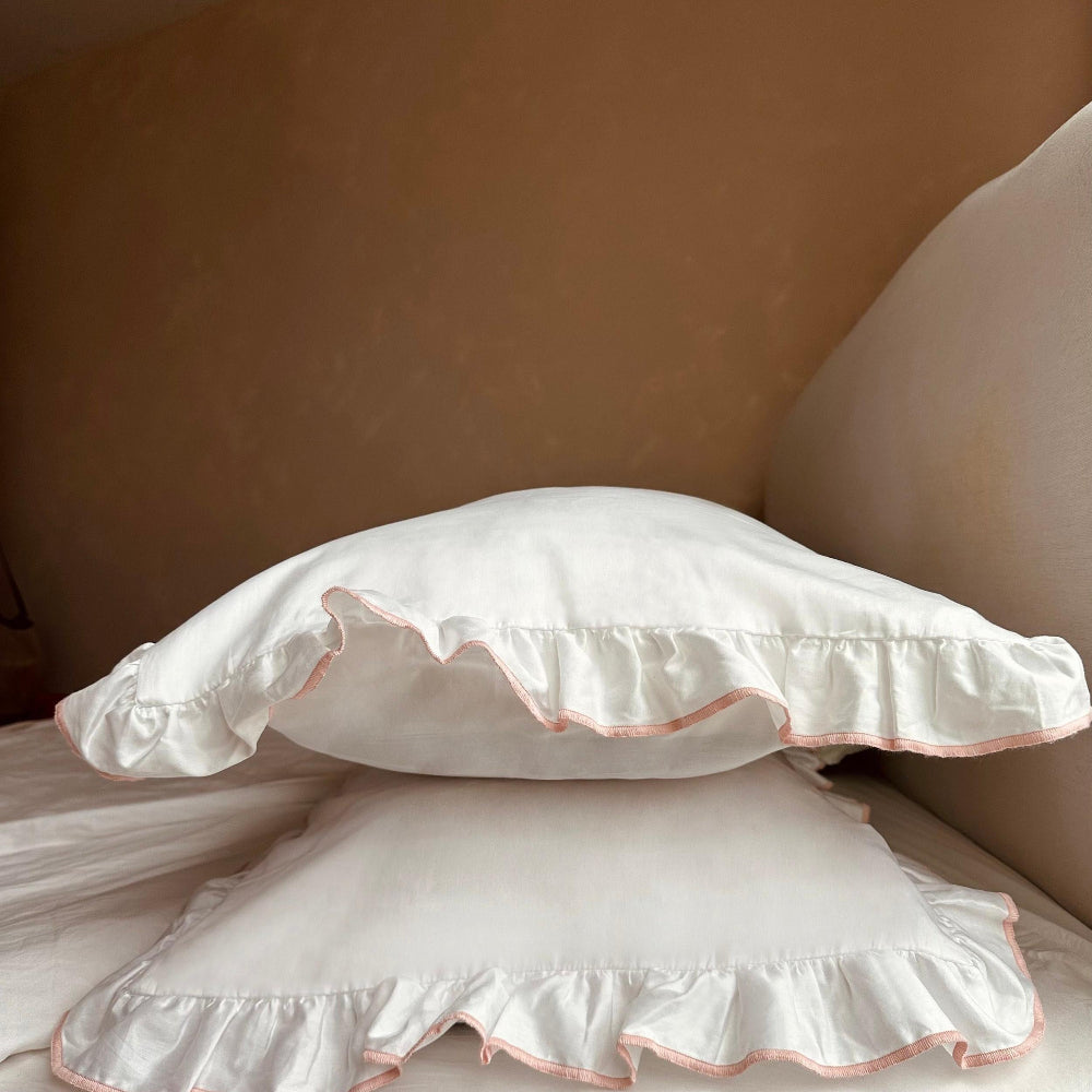 Two white pillows with ruffled edges on a bed against a beige wall.