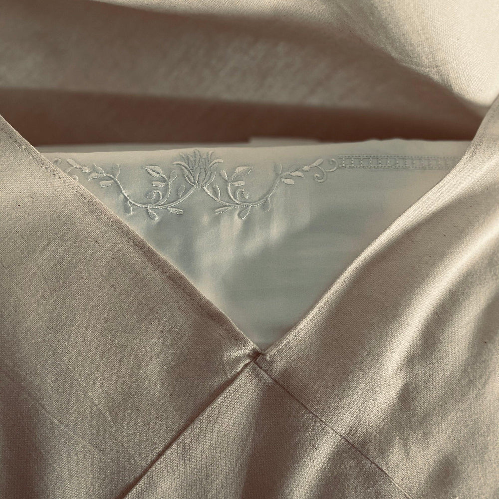 Close-up of beige bedding dust bag with floral embroidery on a white bedding