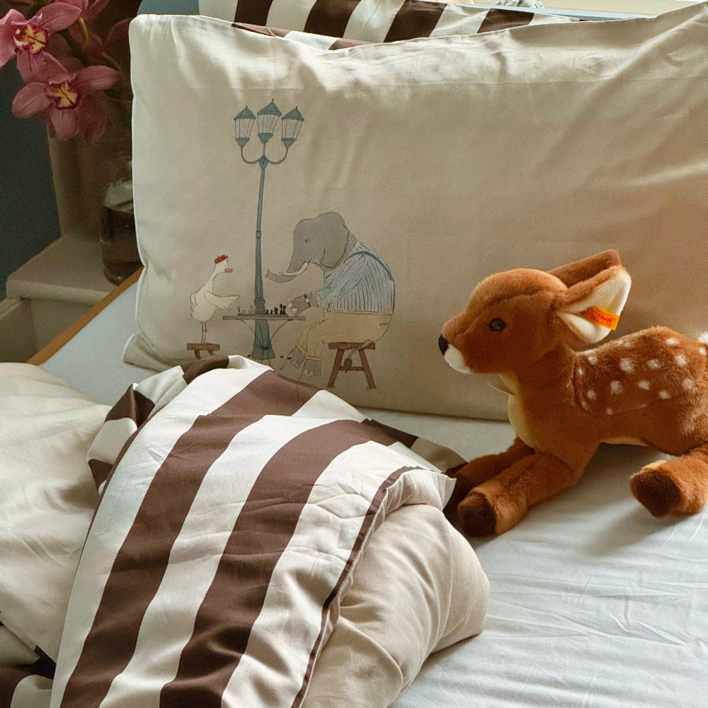 Plush deer toy on a bed with a decorative pillow featuring cartoon characters.