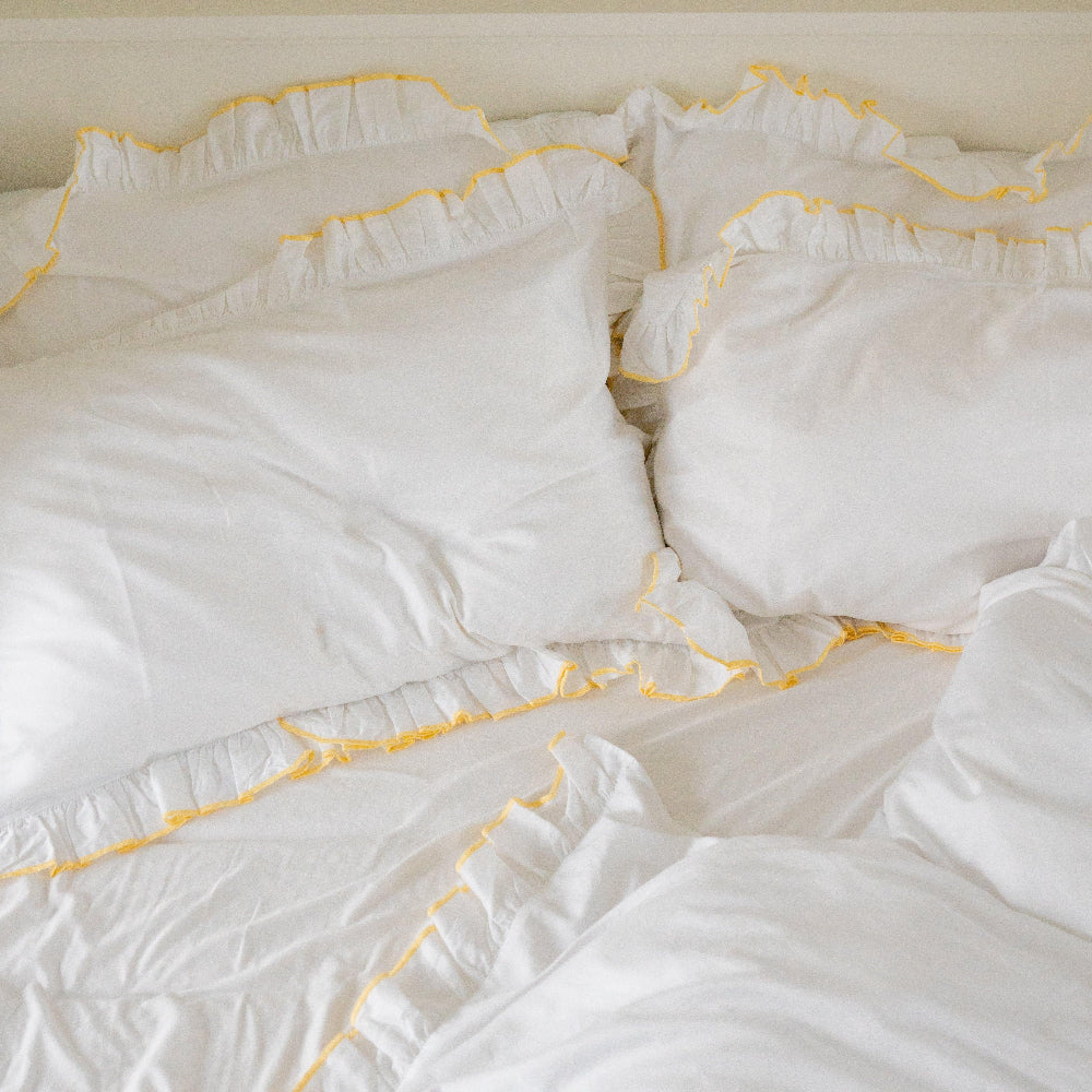 White bedding with yellow trim on a neutral background
