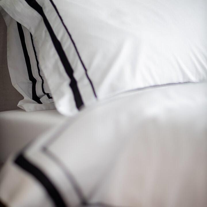 Close-up of white pillows with black stripes on a bed.