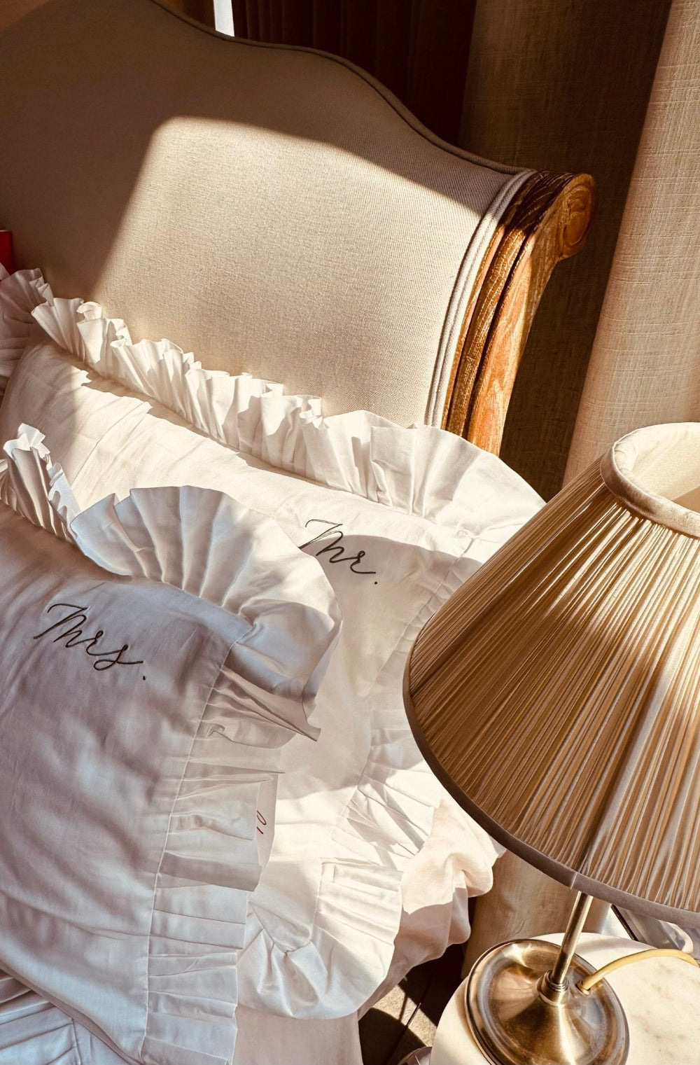 White ruffled fabric with 'Mr' & 'Mrs.' embroidery on a chair next to a lamp.