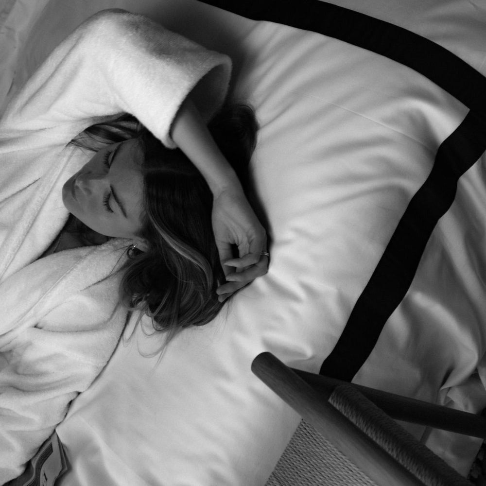 Person lying in bed with a duvet and pillow, black and white photo