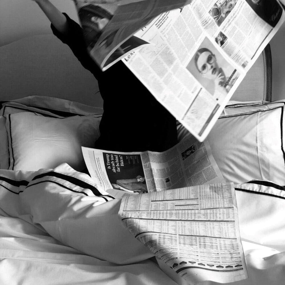 Person lying on a bed with a newspaper spread out over them