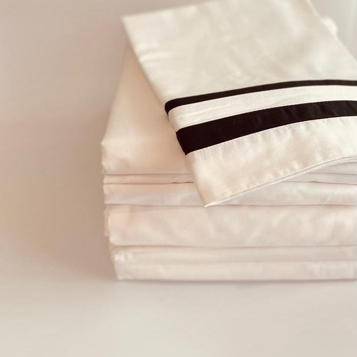 Stack of folded white bedding with black stripes on a light background
