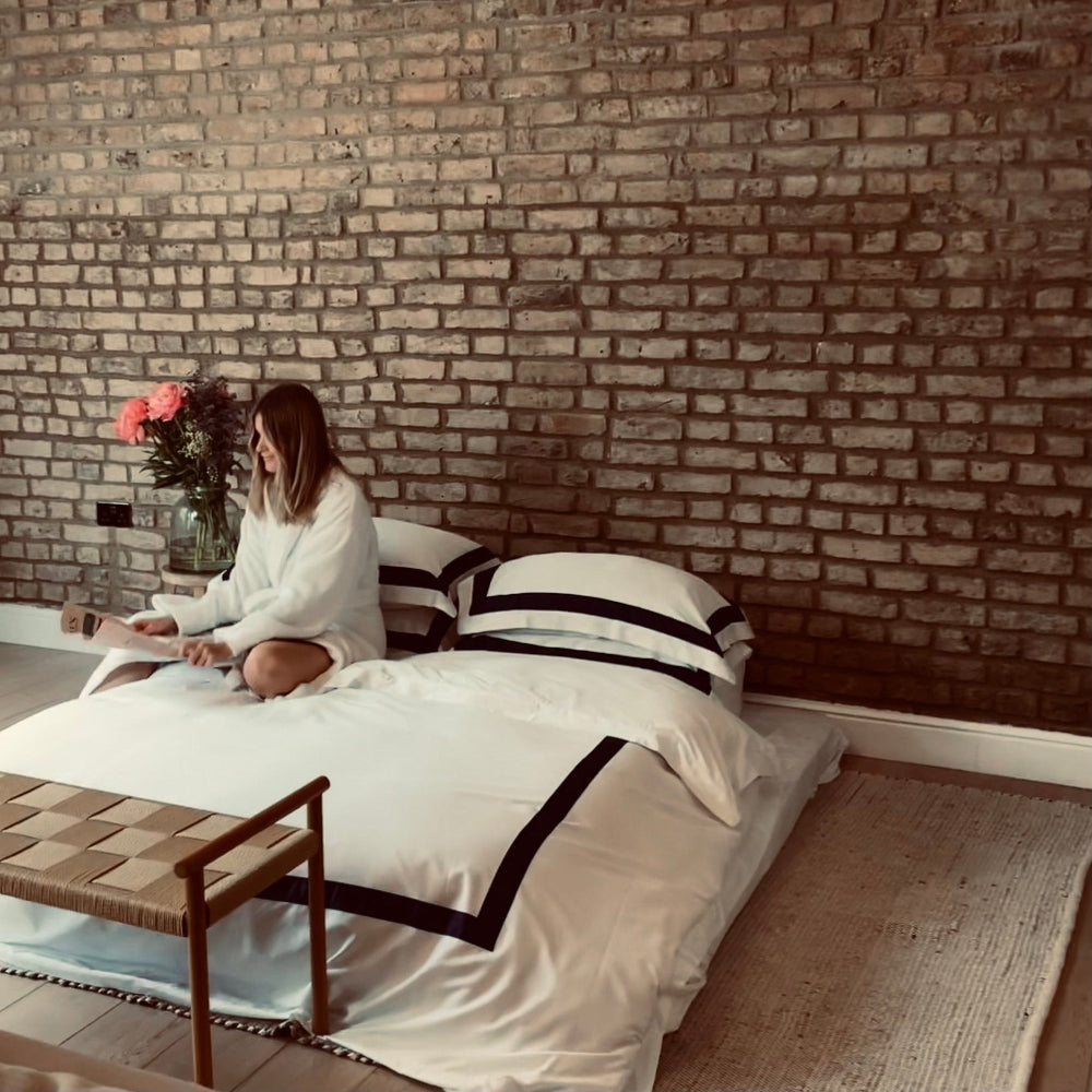 Person sitting on a bed with white bedding against a brick wall
