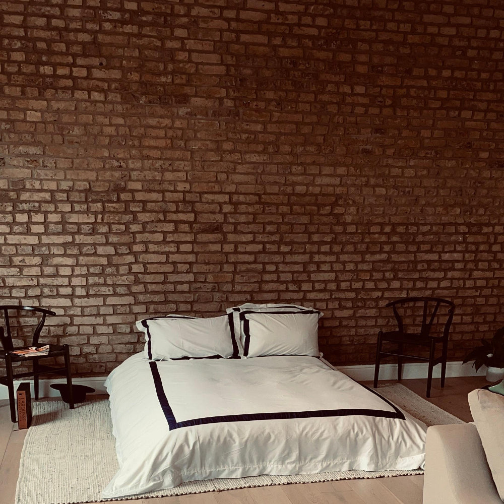 Bedroom with white bedding against a brick wall
