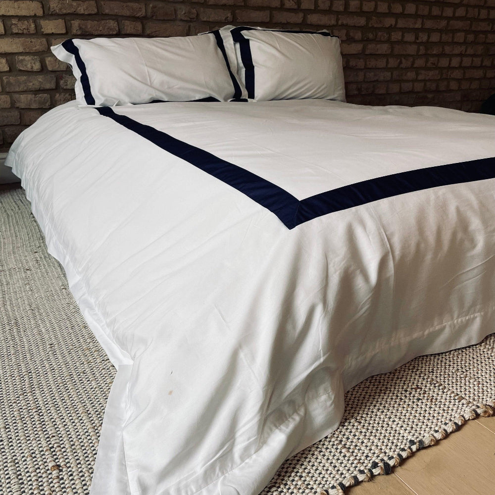 White quilt with navy border on a bed against a brick wall.