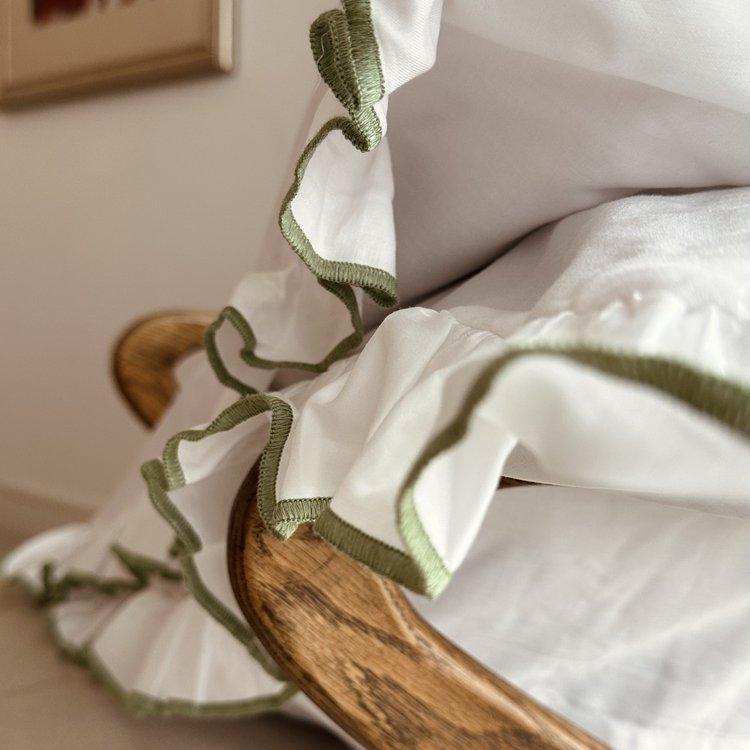 White Pillowcases with green trim draped over a wooden chair.