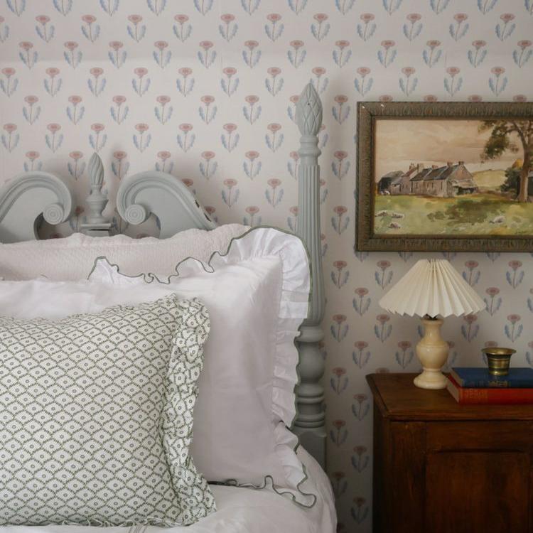 Bedroom with floral wallpaper, bed with white bedding and decorative pillows, and a lamp on a nightstand.
