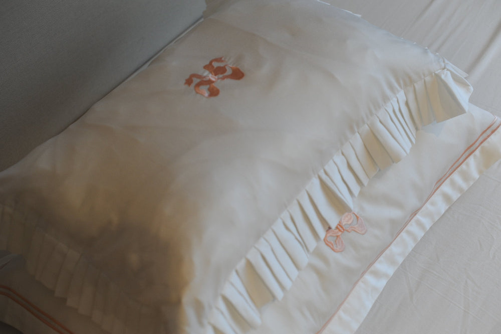 Close-up of embroidered pillowcase with a peach bow on a white background
