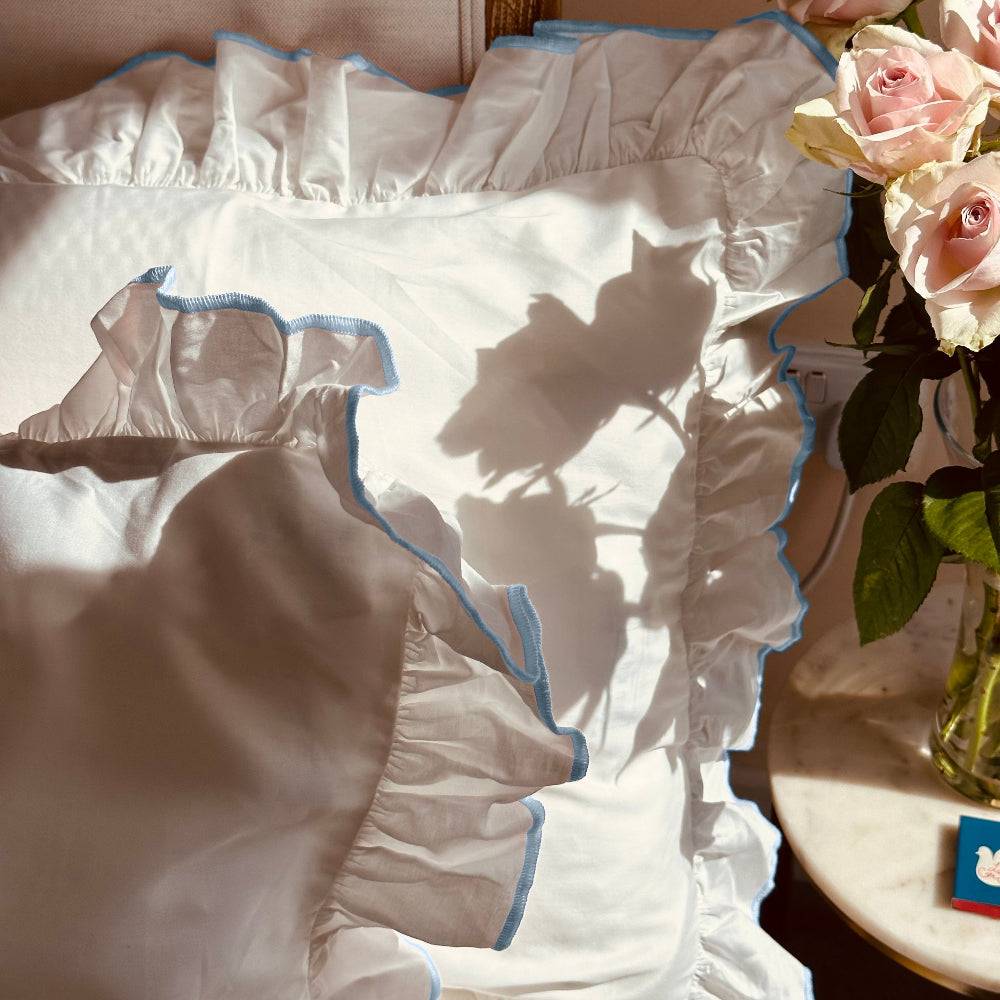 White Provence Bedding set with blue trim on a table next to a vase of roses.