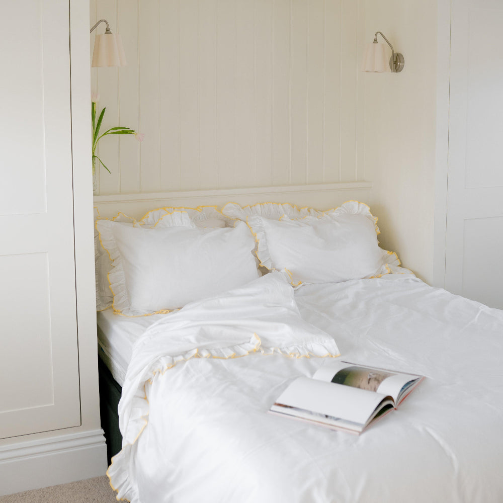 White bed with ruffled bedding and an open book on a light-coloured wall background