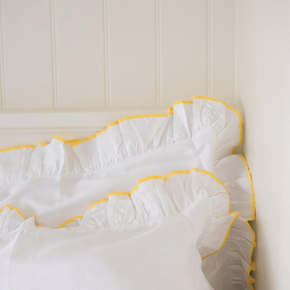 Sukun Provence white pillowcase with butter yellow trim against a beige wall.