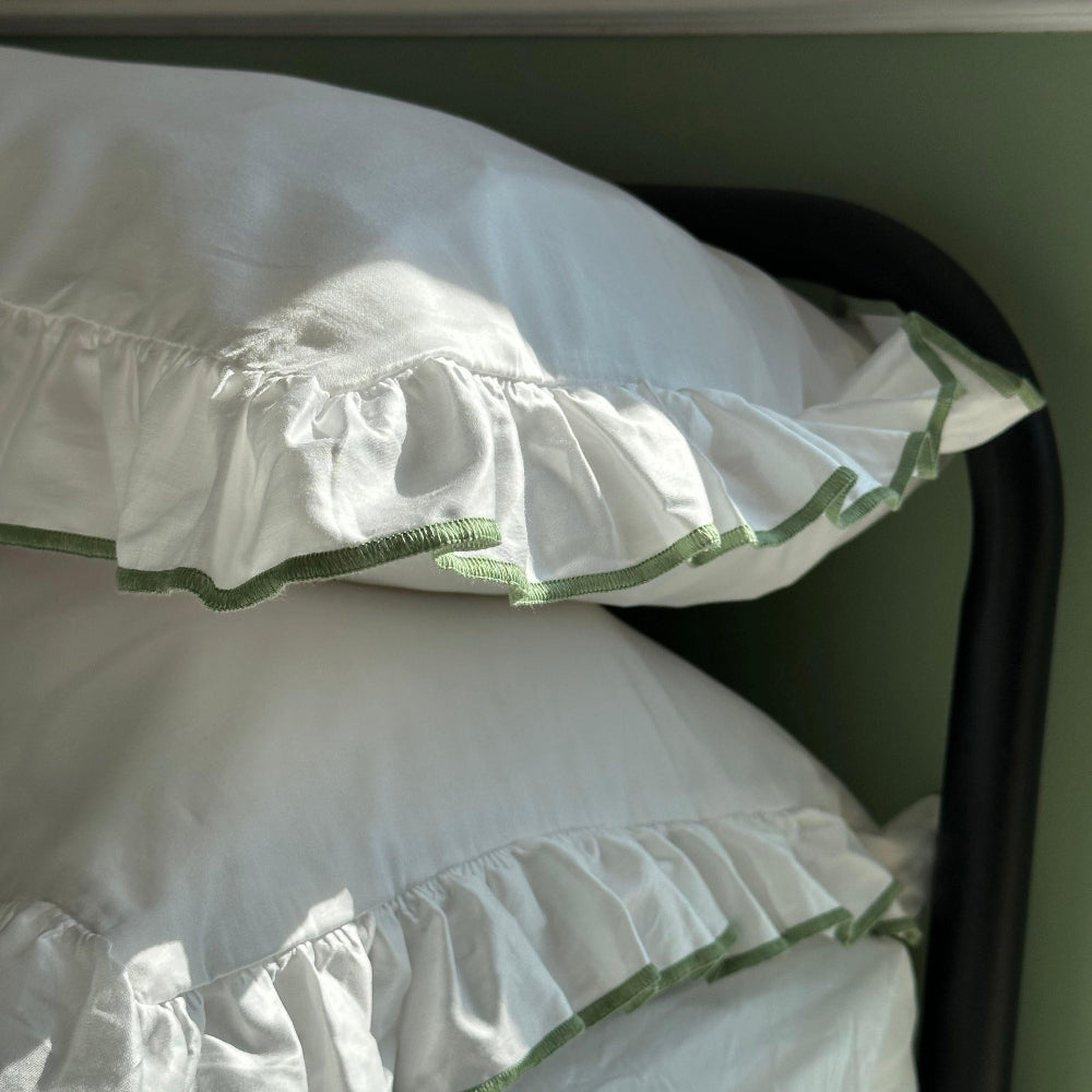 White pillows with green trim on a dark surface against a green wall.