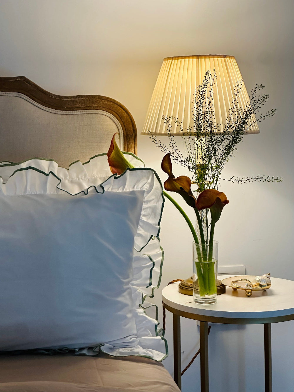 Bedroom scene with a bed, lamp, and small table with flowers.