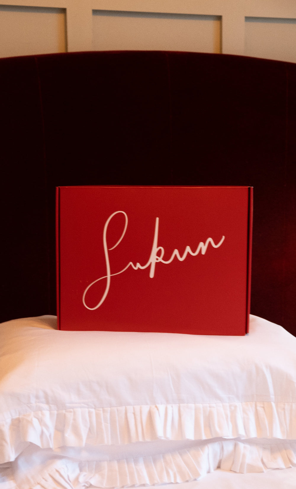 Red box with 'Sukun' branding on a white pillowcase with a dark headboard.