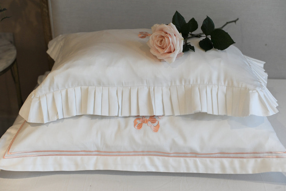 White pillows with ruffled edge and embroidered designs on a neutral background