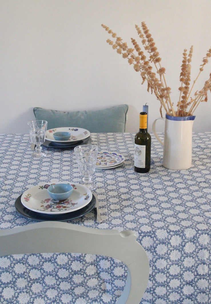 Dining table setting with cotton patterned tablecloth, plates, glasses, and a bottle.
