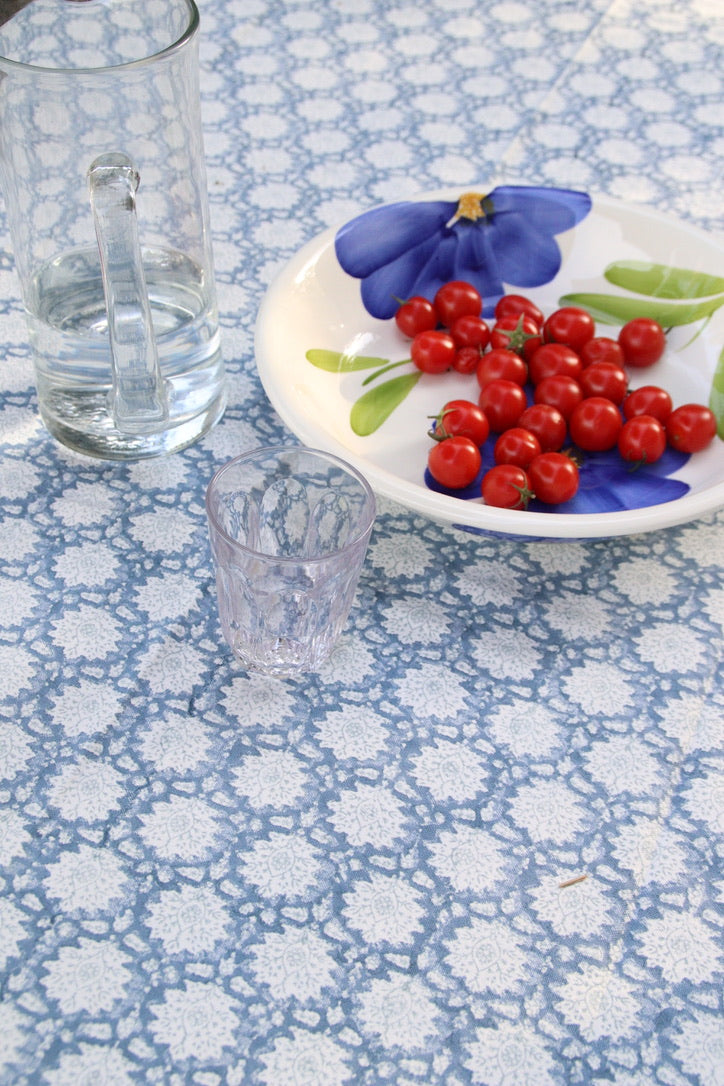 Tablecloth with floral pattern, glass of water, and plate with red berries on a blue and white floral tablecloth.