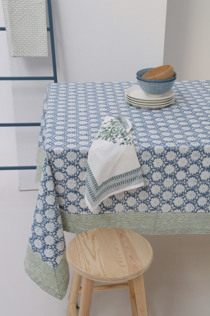 Tablecloth with floral pattern on a table, accompanied by a wooden stool and a stack of plates.