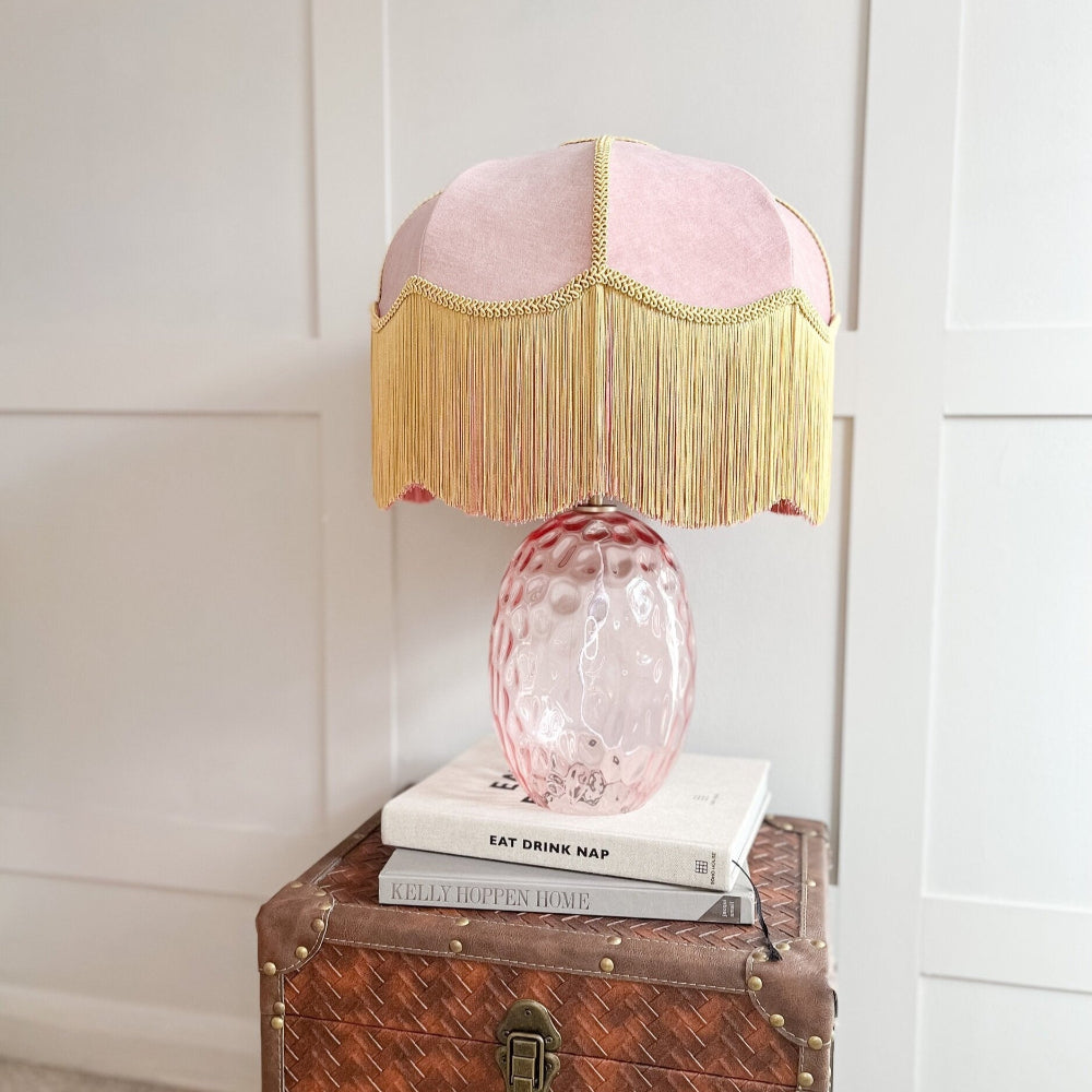 Pink and gold lamp on a wooden chest with a white wall background