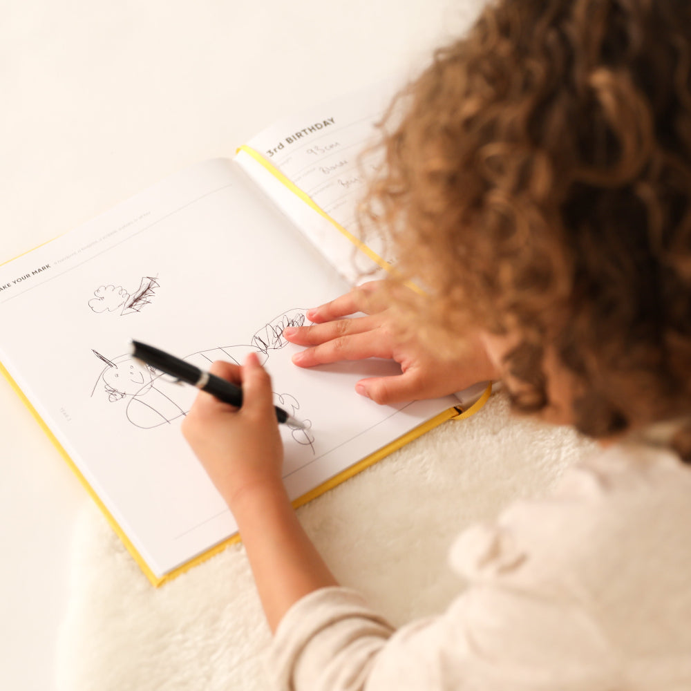 Child drawing with a pen on a piece of paper on the book of you