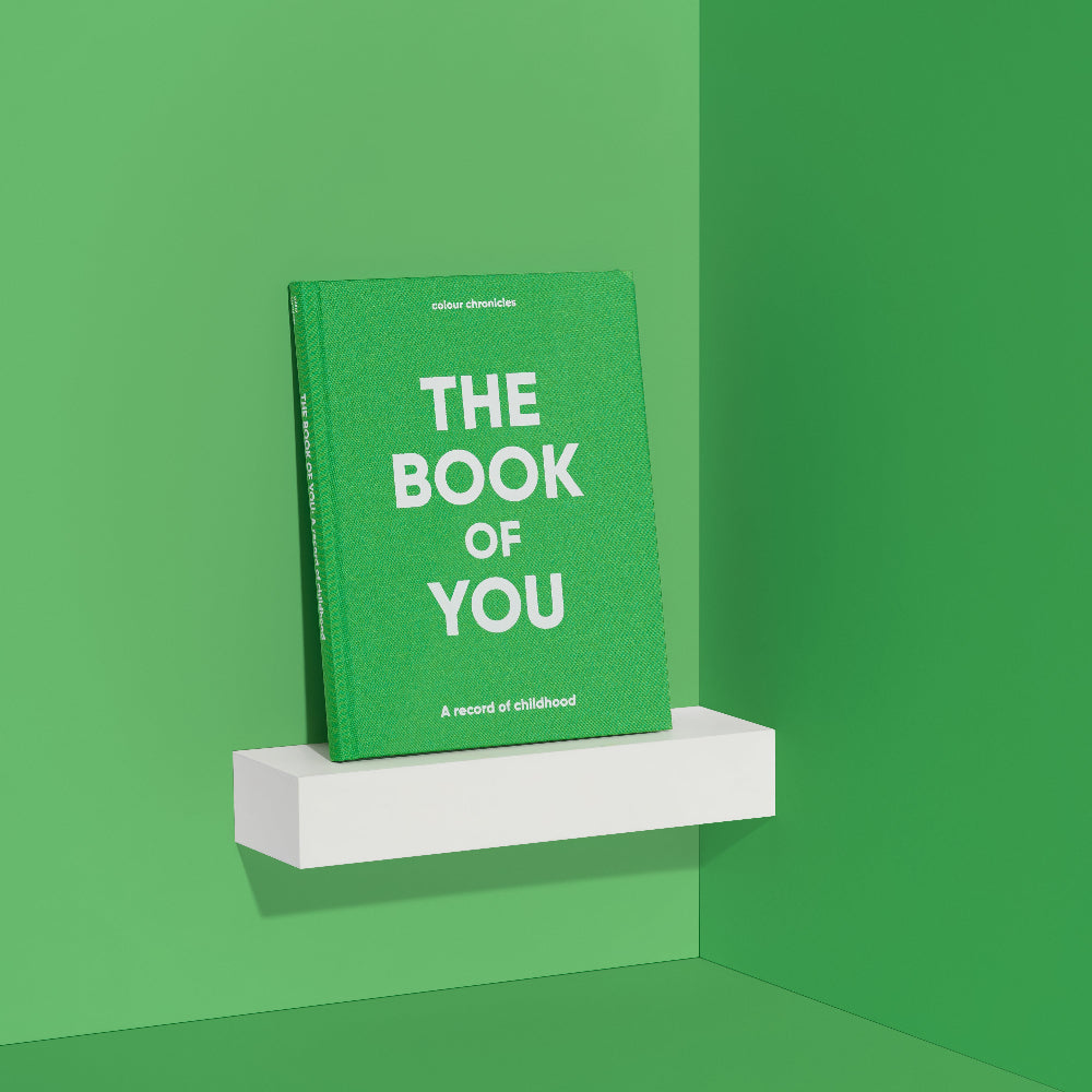 Green book titled 'The Book of You' on a white shelf against a green wall