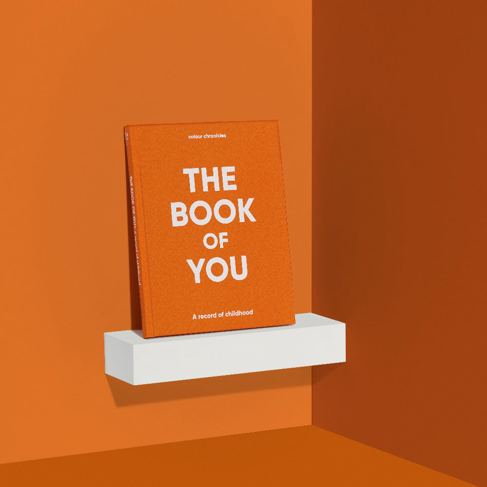 Book titled 'The Book of You' in orange on a white shelf against an orange wall
