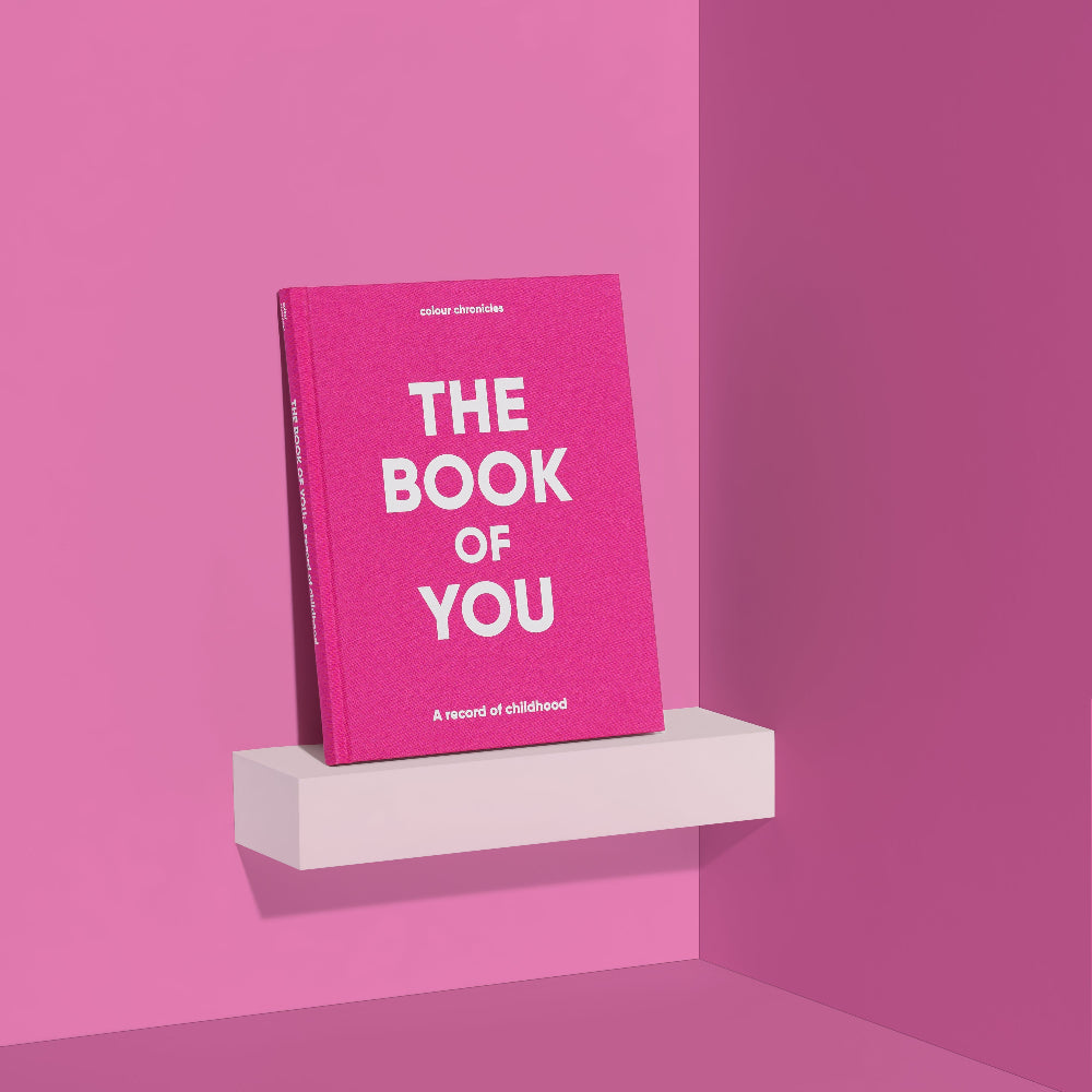 Book titled 'The Book of You' in the colour pink on a white shelf against a pink wall