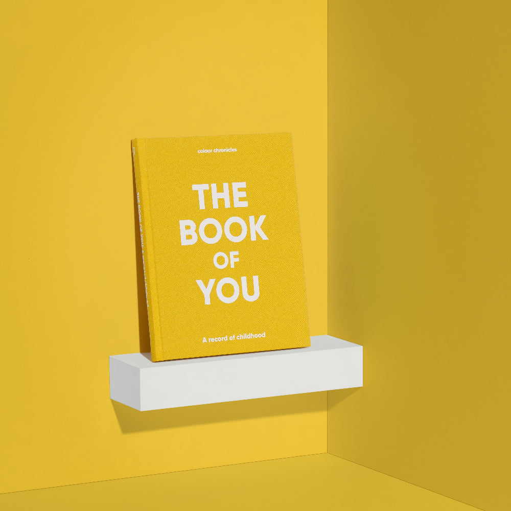 Yellow book titled 'The Book of You' on a white shelf against a yellow wall