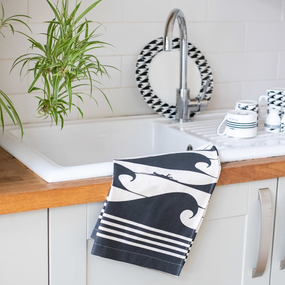 Black and white patterned towel hanging on a kitchen sink with a plant and kitchen items in the background.