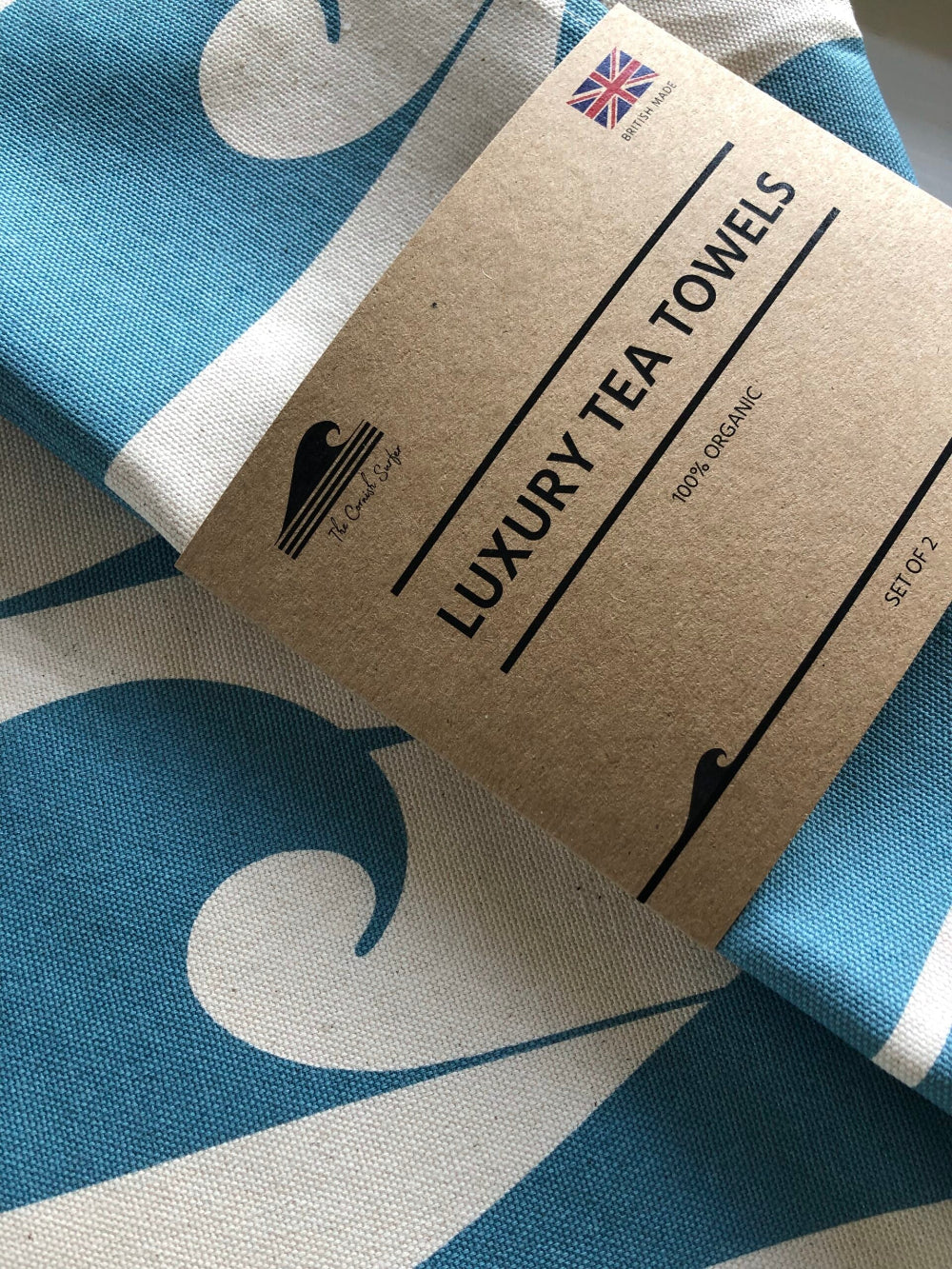 Luxury tea towels with a branded cardboard packaging on a blue and white fabric background.
