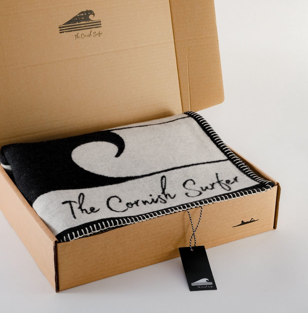 Blanket with 'The Cornish Surfer' branding in a cardboard box on a white background